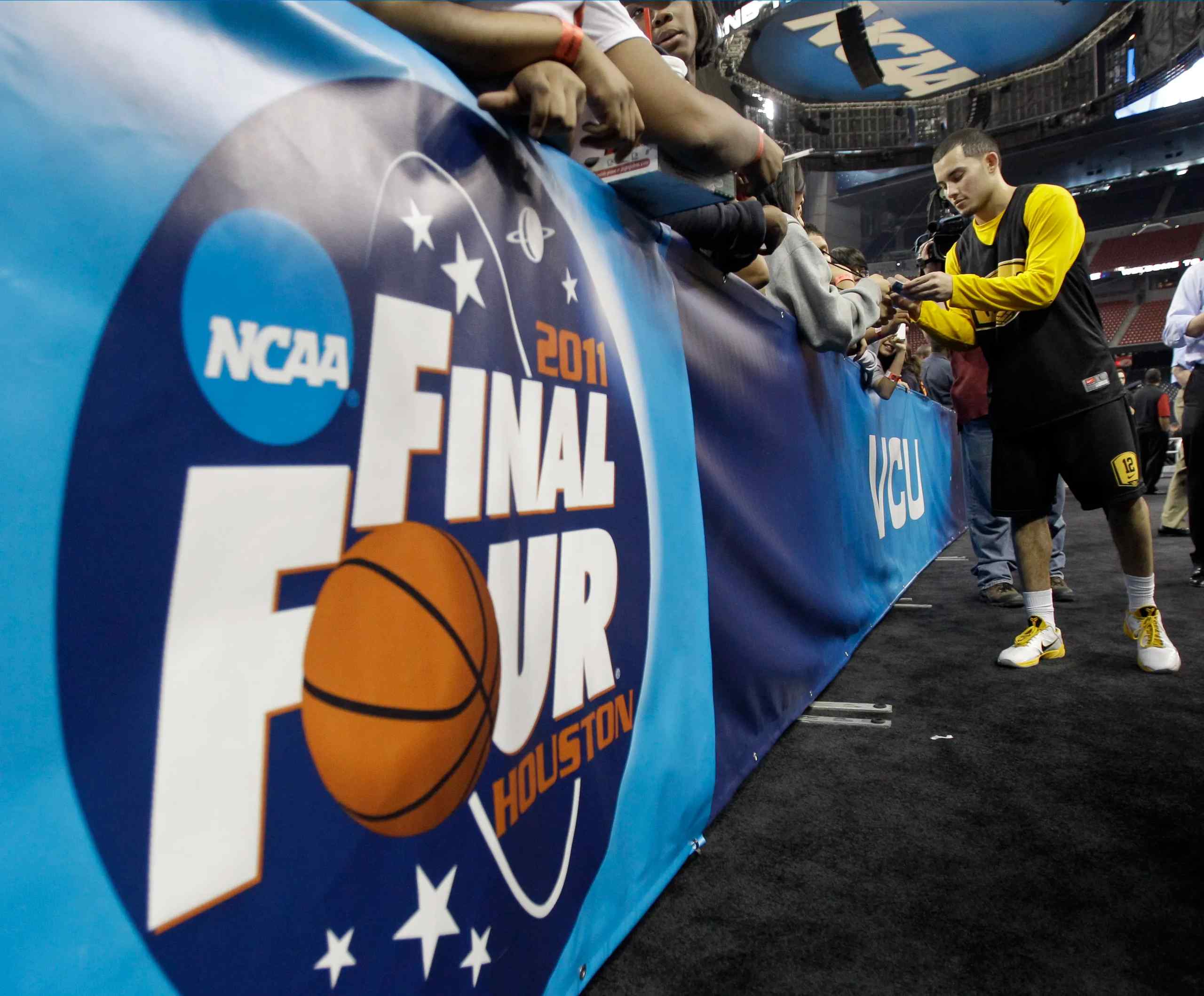 A player signs autographs with a 2011 Final Four banner in the foreground.